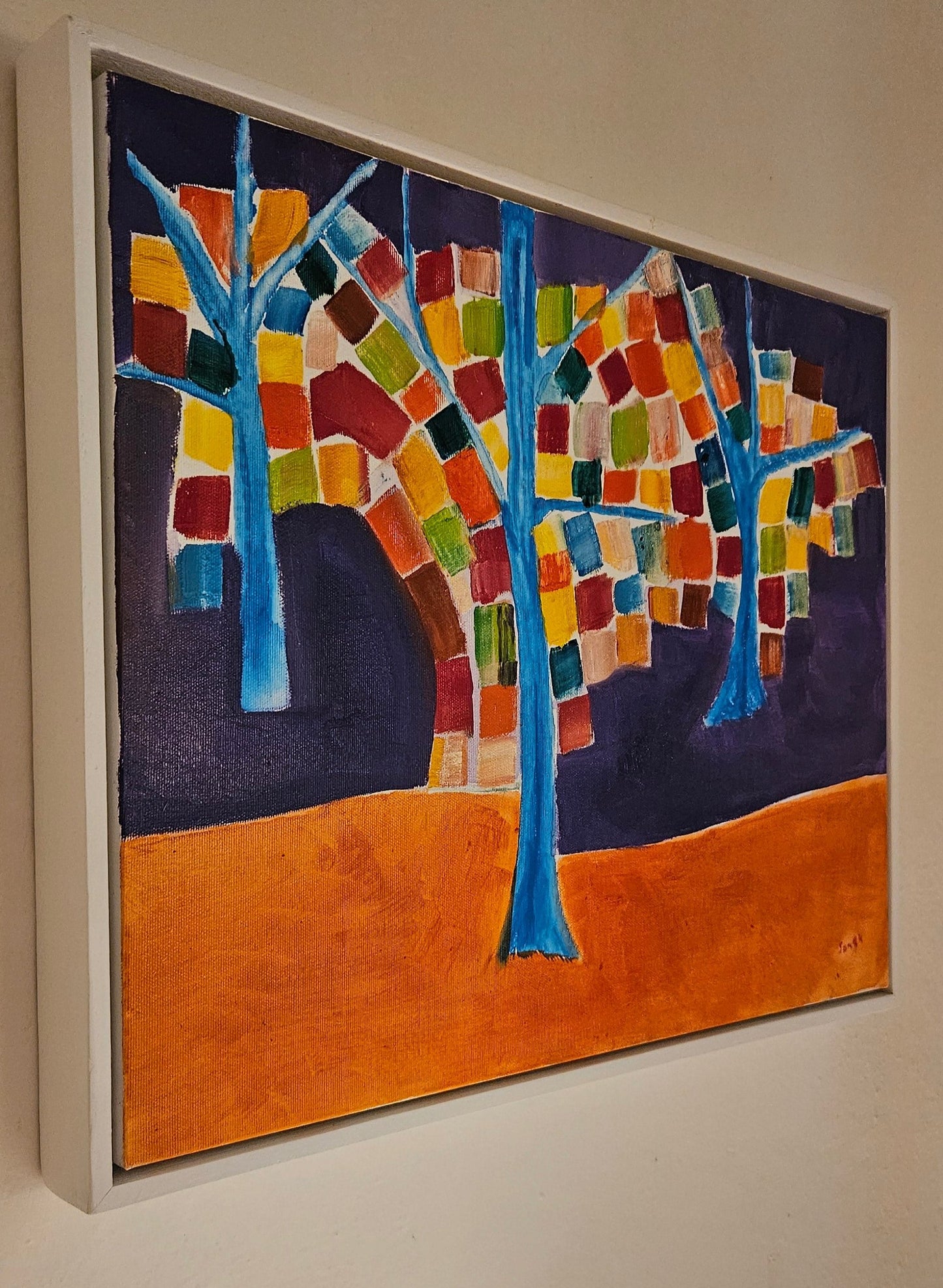 Angled photo of an abstract tree oil painting with 3 trees painted blue with colored square leaves and a purple and orange background. 